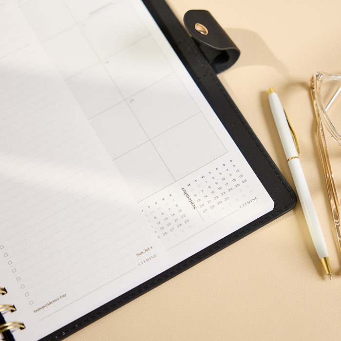 2027 Midnight Plaid Customizable Spiral Citrine Planner - Classic Professional Layout - 12 Months open with monthly calendar pages and white gold pen on a desk
