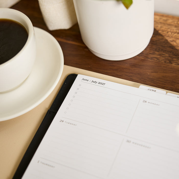 2027 Midnight Plaid Customizable Spiral Citrine Planner - Classic Professional Layout - 12 Months open to a monthly July 2027 spread beside coffee on a wooden desk