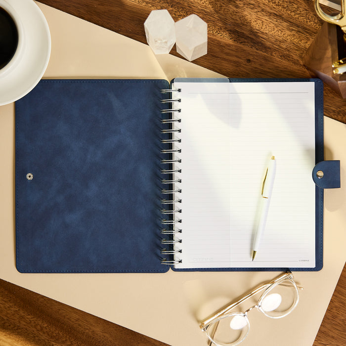 Citrine - Navy - Classic Customizable Spiral Notebook open to lined pages with a white pen on a desk beside glasses and a cup of coffee