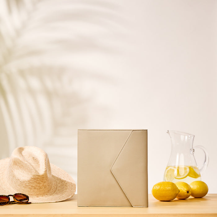 Taupe Vegan Leather - Deluxe Classic Planner Folio standing upright on a wooden surface next to a straw hat, sunglasses, and a pitcher of lemon water with fresh lemons.