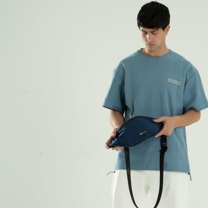 Man wearing blue shirt holding blue crossbody waist pack with black strap