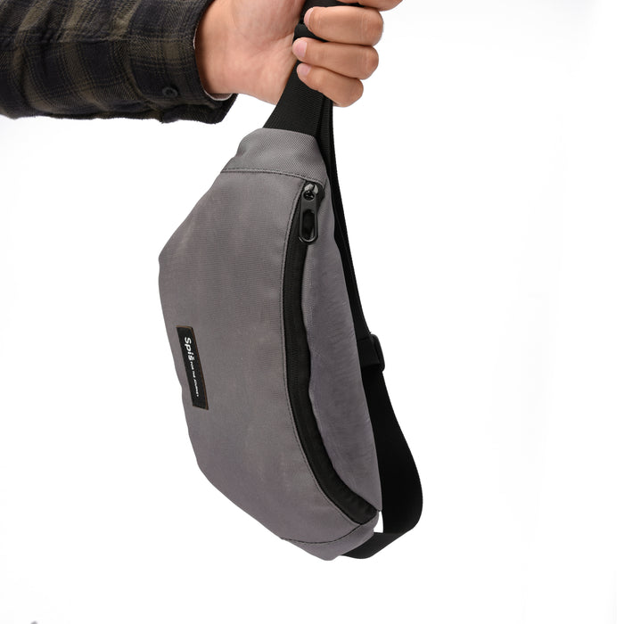 Hand holding a gray crossbody sling bag with black zipper and minimal label