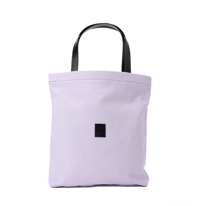 Light purple canvas tote bag with black handles and a small black front patch, isolated on white