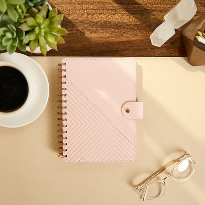 2027 Blush Diagonals Customizable Spiral Citrine Planner - Small Professional Layout - 12 Months, blush pink planner with geometric diagonal cover design and spiral binding beside glasses and coffee
