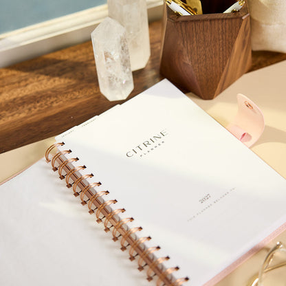 2027 Blush Diagonals Customizable Spiral Citrine Planner - Small Professional Layout - 12 Months shown on a desk with copper spiral binding and white cover