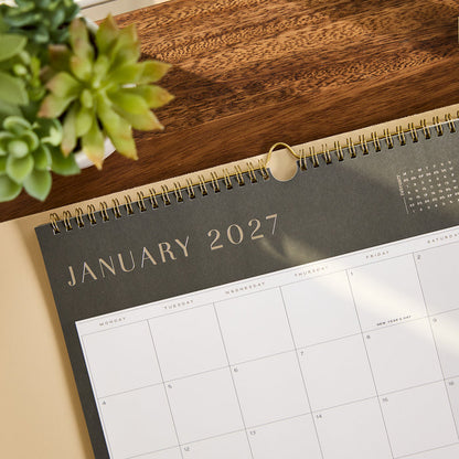 2027 Midnight Citrine Wall Calendar - Small - 12 Months open to January 2027 with a minimalist monthly grid on a wooden desk beside a succulent plant