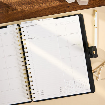 2027 Midnight Customizable Spiral Citrine Planner - Classic Professional Layout - 12 Months open to monthly calendar pages with goals priorities and to do list sections on a desk