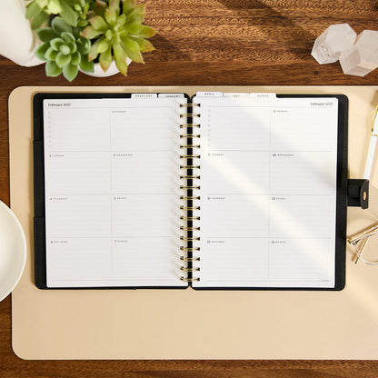2027 Midnight Customizable Spiral Citrine Planner - Classic Professional Layout - 12 Months open to a February 2027 monthly spread on a desk