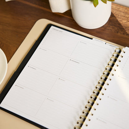 2027 Midnight Customizable Spiral Citrine Planner - Classic Professional Layout - 12 Months opened to a clean monthly planning spread with spiral binding on a desk