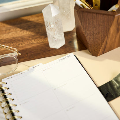 2027 Midnight Micro Dots Customizable Spiral Citrine Planner - Small Professional Layout - 12 Months open on a wooden desk with crystal decor and glasses
