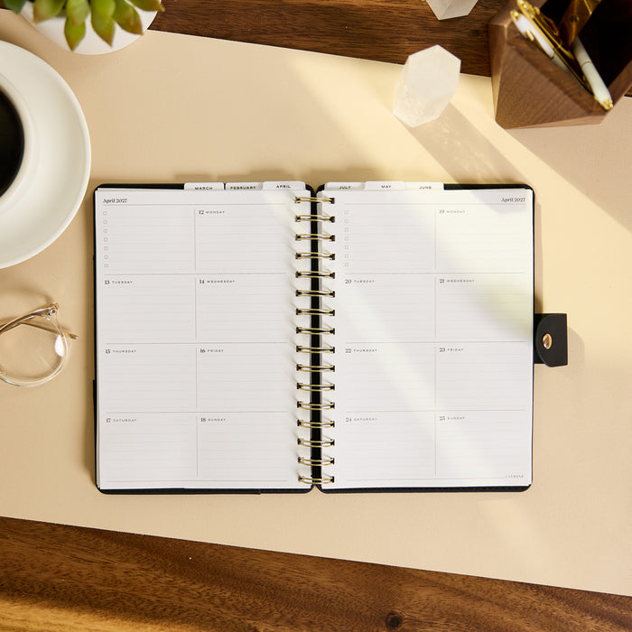 2027 Midnight Plaid Customizable Spiral Citrine Planner - Small Professional Layout - 12 Months open to a monthly planning spread beside a coffee cup