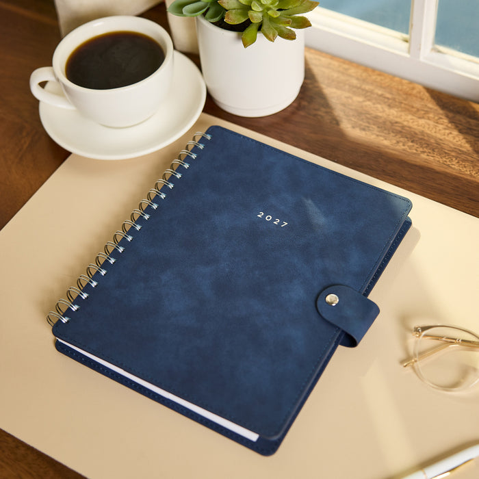2027 Navy Customizable Spiral Citrine Planner - Classic Professional Layout - 12 Months shown on a desk beside coffee and a potted succulent