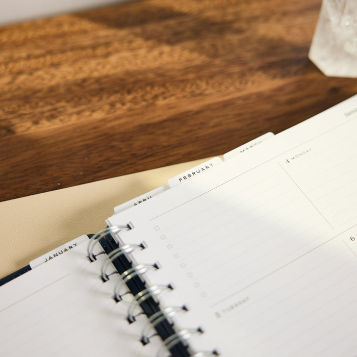2027 Navy Customizable Spiral Citrine Planner - Classic Professional Layout - 12 Months open on a wooden desk with January and February pages and spiral binding
