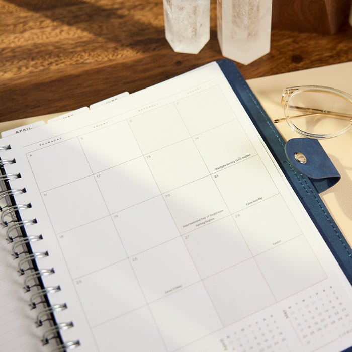 2027 Navy Customizable Spiral Citrine Planner - Classic Professional Layout - 12 Months opened to a monthly calendar spread on a wooden desk