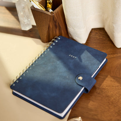 2027 Navy Customizable Spiral Citrine Planner - Small Professional Layout - 12 Months navy spiral planner with snap closure resting on a wooden desk