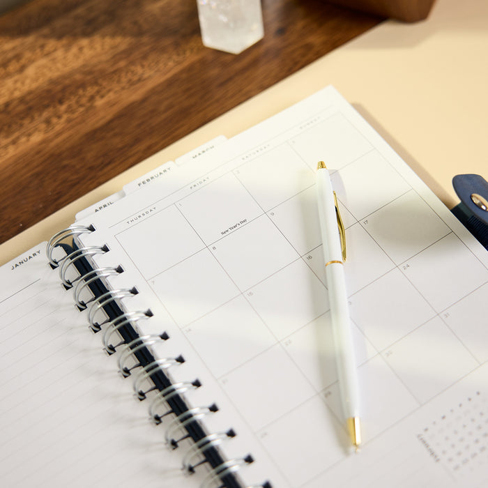 2027 Navy Customizable Spiral Citrine Planner - Small Professional Layout - 12 Months open to a monthly calendar with a pen