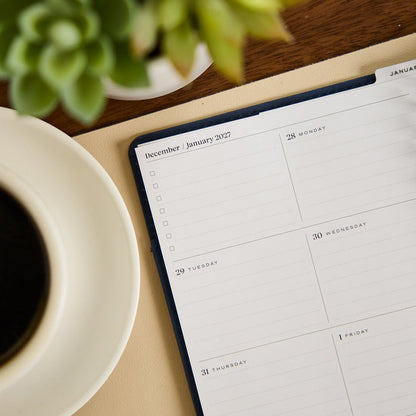2027 Navy Customizable Spiral Citrine Planner - Small Professional Layout - 12 Months shown open to January 2027 calendar pages beside coffee and a plant
