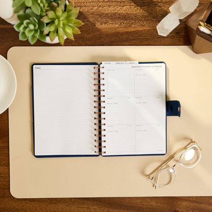 2027 Navy Herringbone Customizable Spiral Citrine Planner - Small Professional Layout - 12 Months open on a desk with monthly planning pages and navy cover
