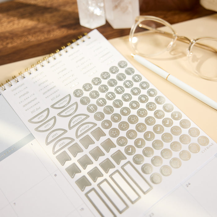 2027 Soft Frame Citrine Wall Calendar - Small - 12 Months with neutral planner stickers arranged on an open calendar page beside glasses and a pen
