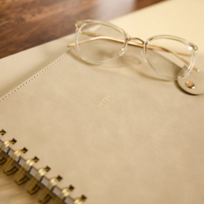 Citrine - Mocha - Classic Customizable Spiral Notebook with a mocha cover and gold spiral binding, photographed with eyeglasses resting on top