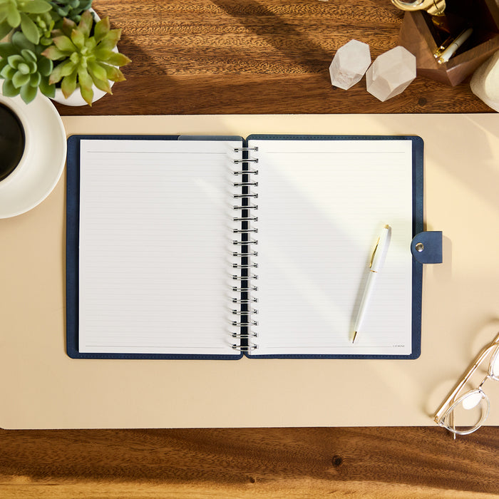 Citrine - Navy - Classic Customizable Spiral Notebook open on a desk with lined pages and a white pen ready for writing beside a coffee cup and plant