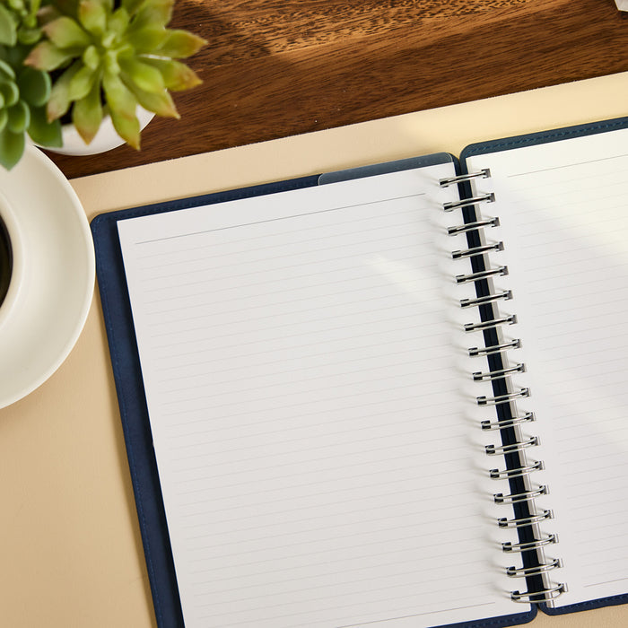 Citrine - Navy - Classic Customizable Spiral Notebook open to blank lined pages on a desk beside a plant and coffee cup