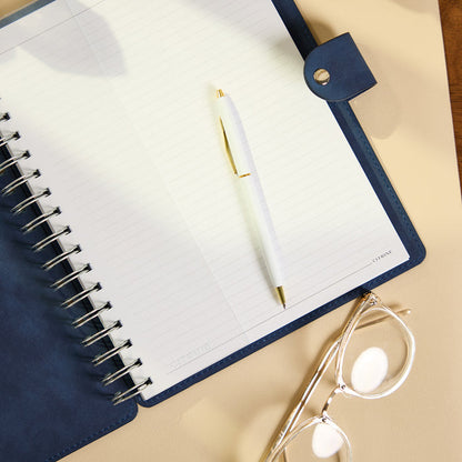 Citrine - Navy - Classic Customizable Spiral Notebook open with lined pages a white pen and reading glasses on a warm neutral surface