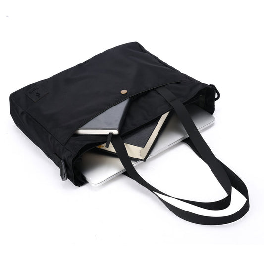 Black tote bag with books, notebook, and laptop on white background