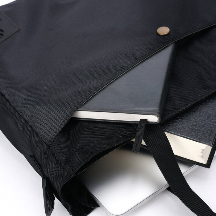 Black tote bag with notebook, book, and laptop partially visible inside