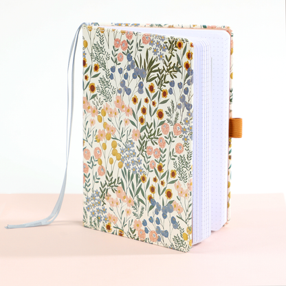 Ditsy Wildflower - Bullet Dot Grid Happy Journal® - 80 Sheets - 160gsm Paper with a floral cover design, featuring a bookmark ribbon and pen loop, standing open on a light surface.