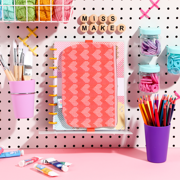Miss Maker - Classic Banded Pen Pouch in coral pink with a heart pattern, displayed on a pegboard with colored pencils, paintbrushes, and craft supplies for planners and journals.