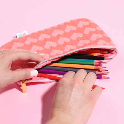 Person’s hands opening a coral patterned Miss Maker - Classic Banded Pen Pouch filled with colorful sharpened pencils on a pink background