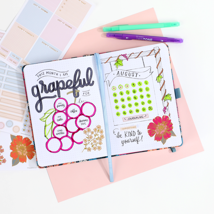 Open Retro Blooms - Bullet Dot Grid Happy Journal® - 80 Sheets - 160gsm Paper with hand-drawn gratitude list, calendar, and floral doodles, next to pastel stickers and colorful pens.