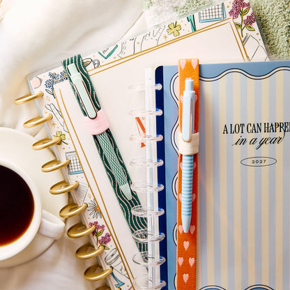 Screen Free Society - Elastic Band Pen Holder - 2 Pack shown with green and orange elastic pen holders attached to disc bound planners beside a coffee cup