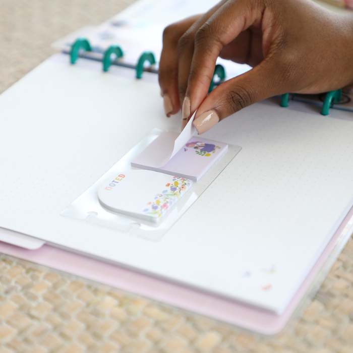 Hand peeling a floral sticky note from a pack placed on a dot grid filler paper inside a disc-bound planner, featuring the Squad Goals Love Every Season - Classic Accessory Pack.