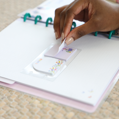 Hand peeling a floral sticky note from a pack placed on a dot grid filler paper inside a disc-bound planner, featuring the Squad Goals Love Every Season - Classic Accessory Pack.