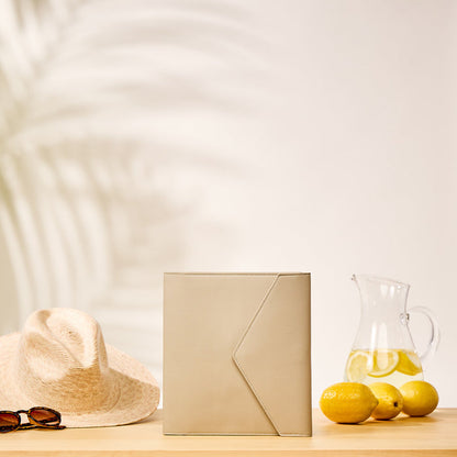 Taupe Vegan Leather - Deluxe Classic Planner Folio standing upright on a wooden surface next to a straw hat, sunglasses, and a pitcher of lemon water with fresh lemons.