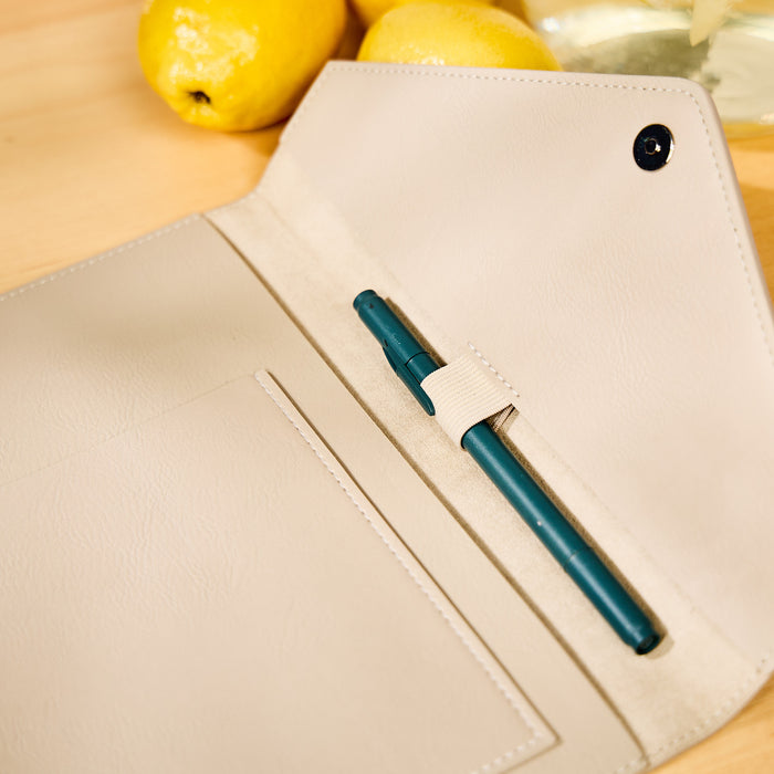 Taupe Vegan Leather - Deluxe Classic Planner Folio opened to show pen holder with teal pen, interior pocket, and soft vegan leather material on wooden surface with lemons nearby.