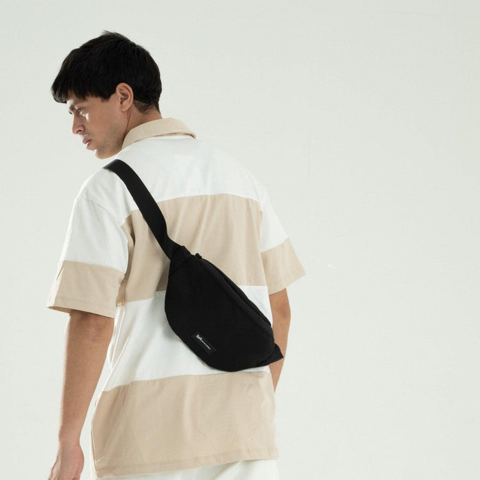 Man wearing a black cross bag waist pack over a beige and white striped shirt
