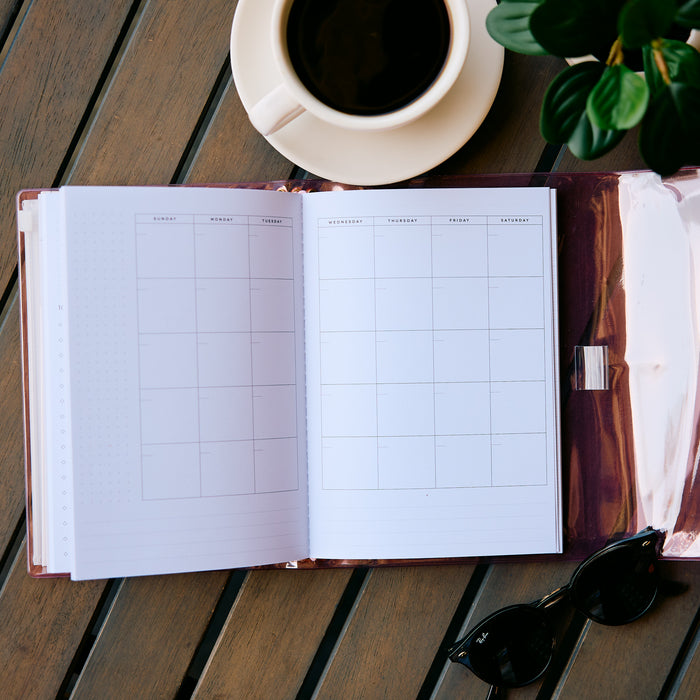 Undated Modern Tones Folio Planner Insert - Monthly Calendar View A5 Layout- 12 Months open to a monthly calendar spread beside coffee and sunglasses