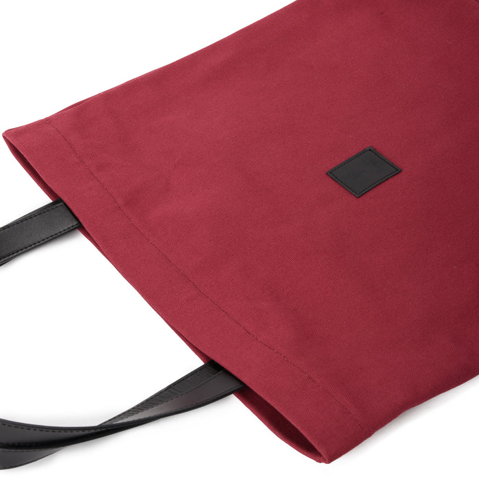 Red canvas tote bag with black faux leather handles on white background