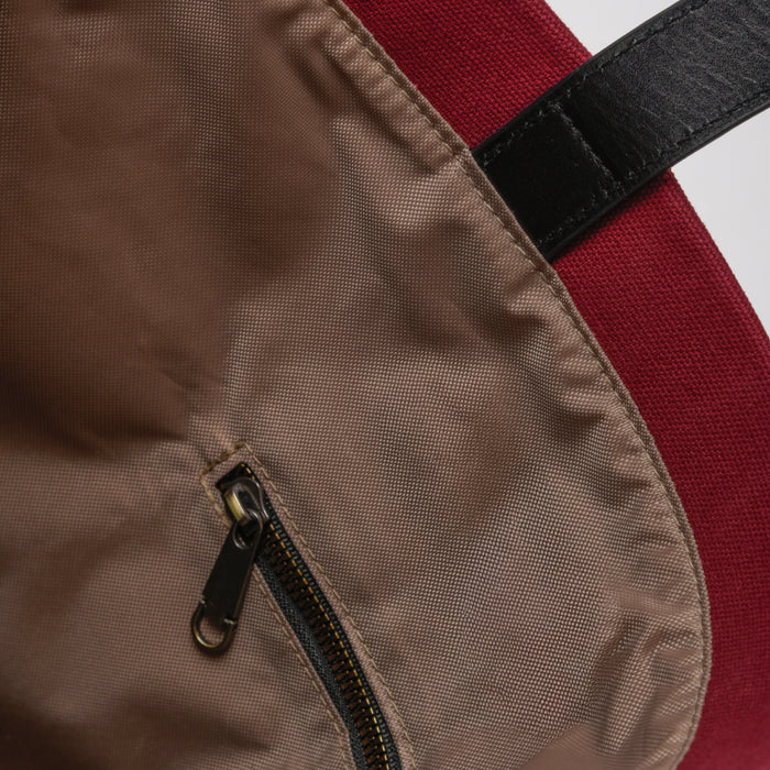 Close-up of brown zipper pocket on red fabric backpack with black strap