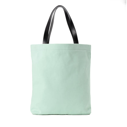 Mint green canvas tote bag with black leather handles on white background