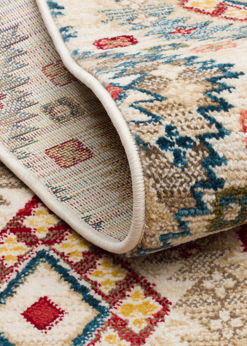 Folded corner of a cream rug featuring a multi-colored geometric pattern in red, blue, and yellow on a white background.