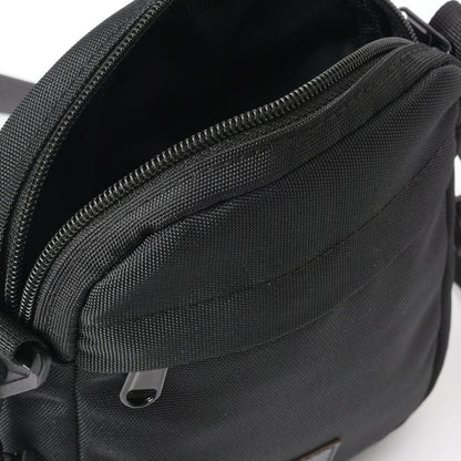 Close-up of black cross bag with zipper, textured fabric, and exterior pocket