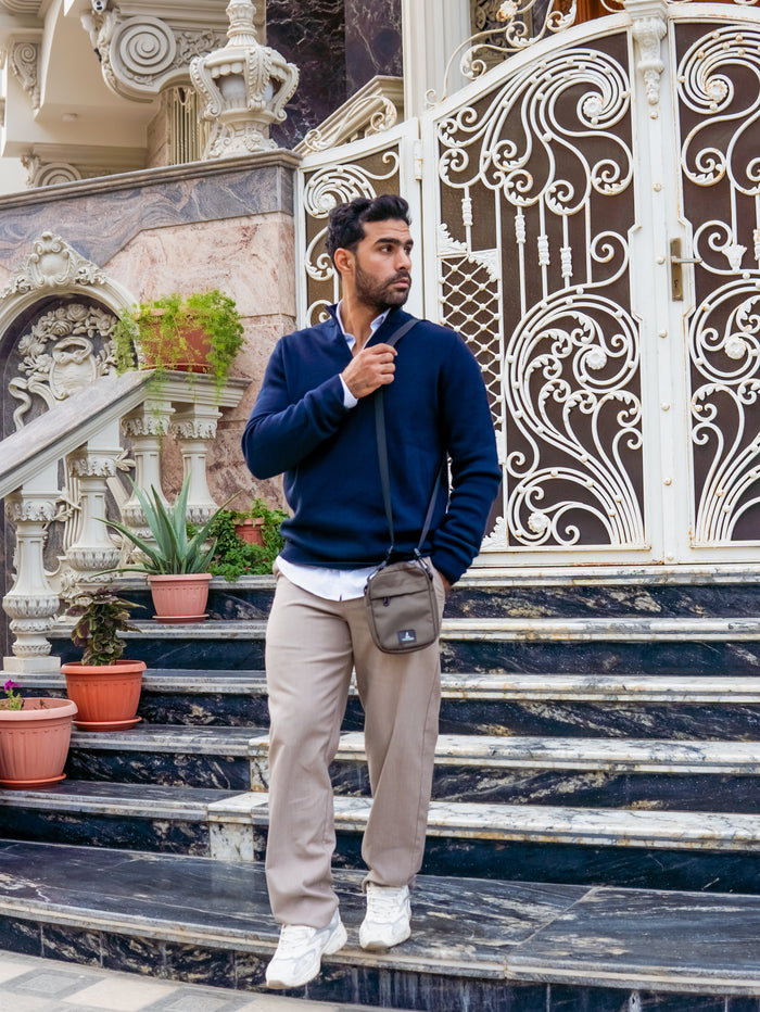 Man in casual outfit with crossbody bag standing on marble steps by ornate gate